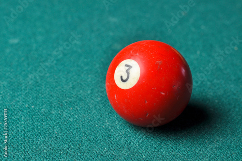 Old billiard ball number 3 red color on green billiard table, copy space