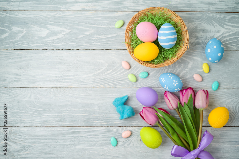 Easter holiday background with easter eggs in basket and tulip flowers on wooden table.