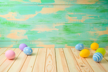 Empty wooden table with Easter eggs over colorful background.