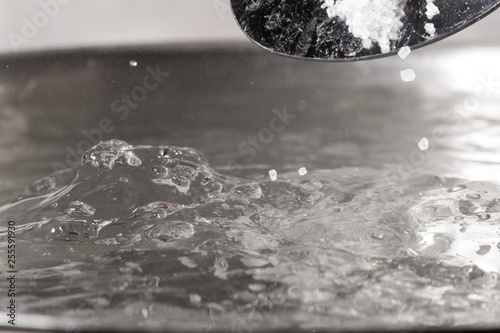 Add salt to boiling water in a metal pan close-up photo