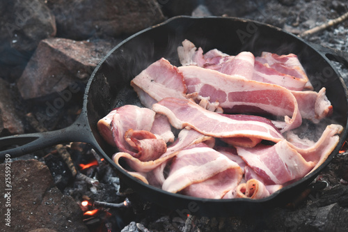 Bacon cooking in cast iron over campfire 