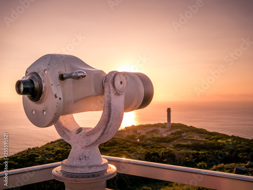 Image of viewpoint with binoculars during colorful sunset pointing at the ocean