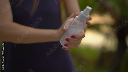 Superslowmotion shot of a beautiful young woman applying an antimosquito repellent spray on her skin. A tropical background. Mosquito defense concept photo