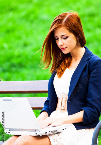 Redhead girl sitting at the bench with notebook