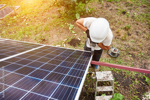 View from above of technician working with screwdriver connecting solar photo voltaic panel to exterior metal platform on sunny day. Alternative renewable ecological green energy sources concept. © anatoliy_gleb