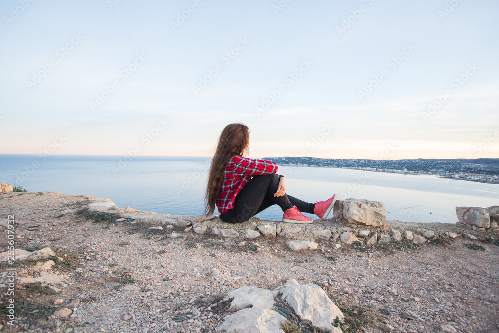 Travel, adventures and loneliness concept - A girl sits on the edge of the cliff and looking the sea