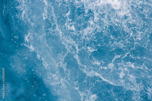 Pale blue sea surface with waves, splash, foam and bubbles at high tide and surf, abstract background