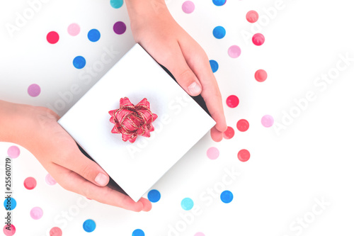 Hands holding a gift box with red bow flower over multicolored confetti. Present and celebration isolated