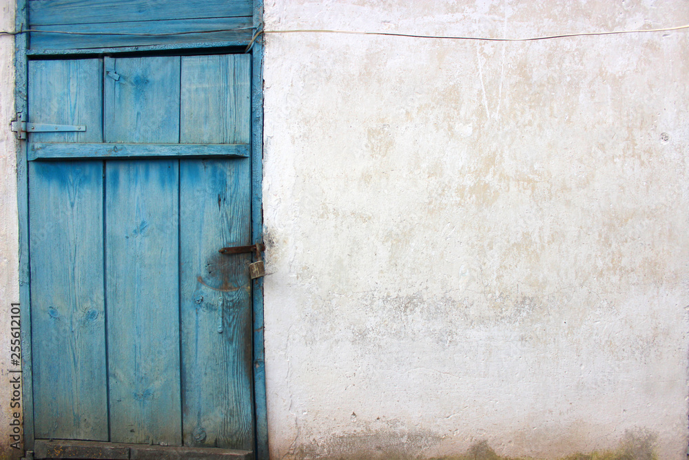 Old padlock. The door is wooden painted in blue. The wall is white, covered with lime.Background.