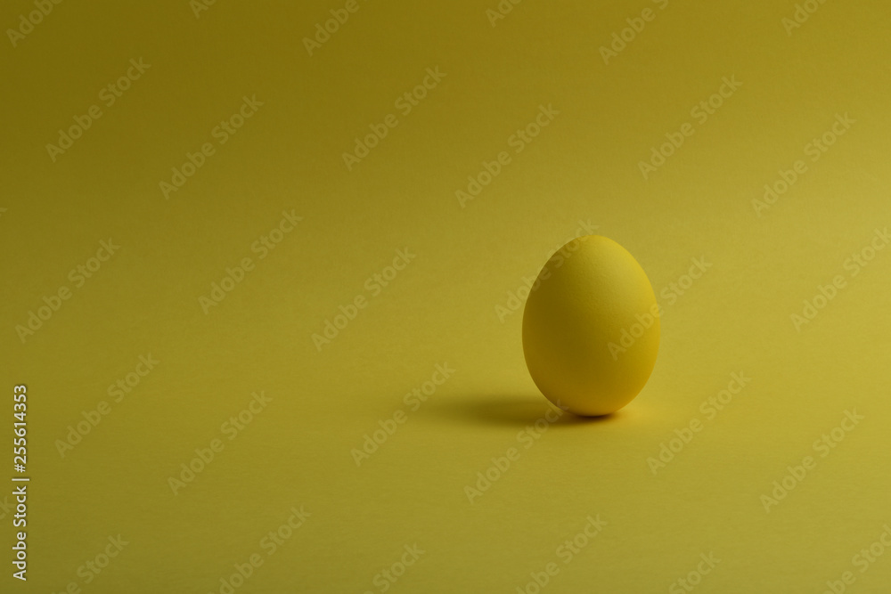 One yellow painted Easter eggs stand on a yellow background. Happy Easter holiday card or banner. Copy space.