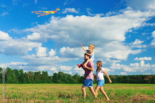 Mother, father and daughter are flying a kite in the field. back view, copy space.