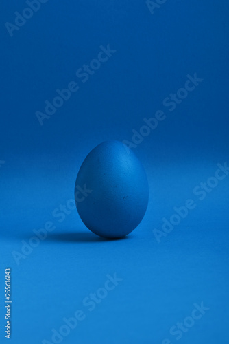 One blue painted Easter egg stand on a blue background. Happy Easter holiday card or banner.