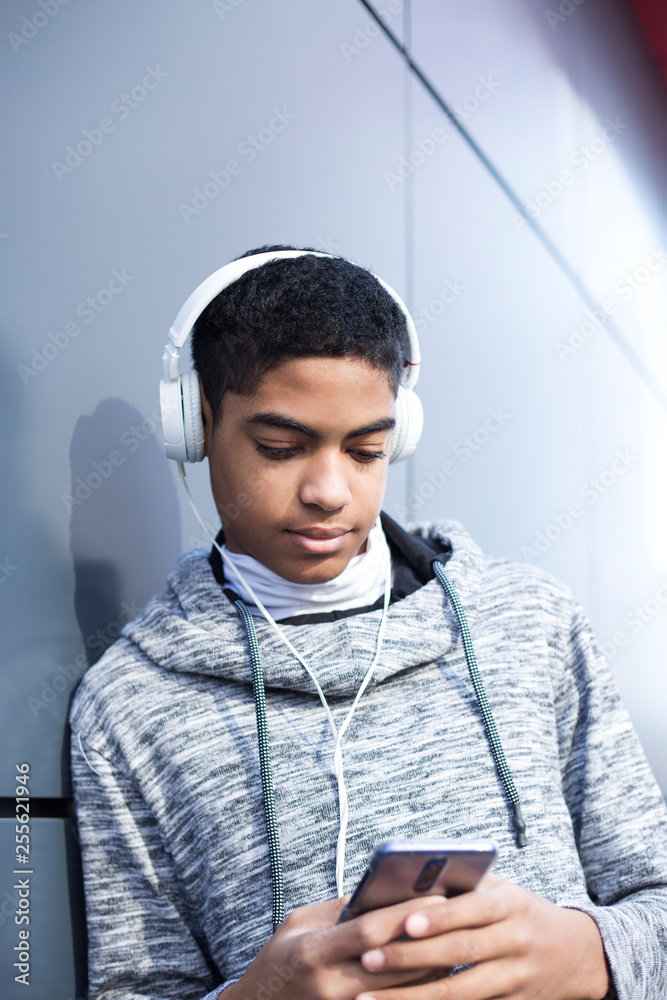 Afro american boy teenager in headphones listening to music on mobile  phone. Cute black man uses smartphone outside. Stock Photo | Adobe Stock