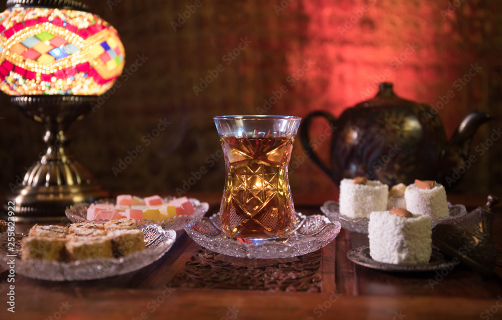 Arabian tea in glass with eastern snacks on vintage wooden surface. Eastern tea concept. Low light lounge interior with carpet. Empty space.