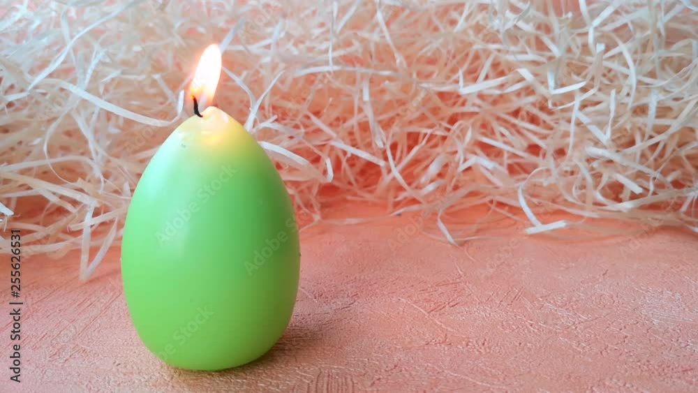 Green candle in the shape of an egg on a background of straw