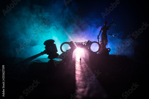 Legal law concept. Silhouette of handcuffs with The Statue of Justice on backside with the flashing red and blue police lights at foggy background. Selective focus © zef art
