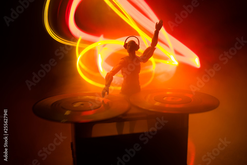 Dj club concept. DJ mixing, and Scratching in a Night Club. Man silhouette on vinyl turntable, strobe lights and fog on background. Creative artwork decoration with toy. © zef art