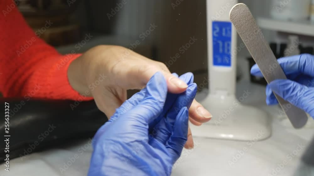 A beautician in protective gloves smoothes his nails with a nail file. A beautician in protective gloves smoothes his nails with a nail file.