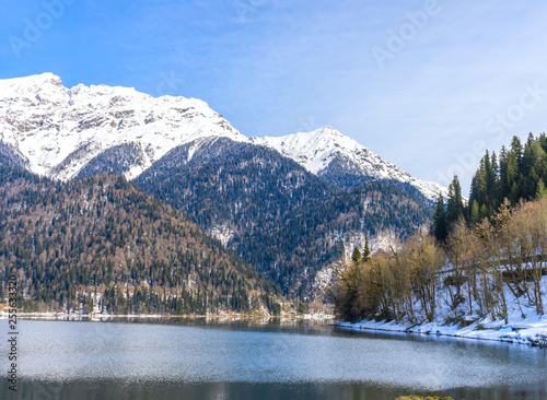 Fototapeta Naklejka Na Ścianę i Meble -  Mountains covered with forests and snow on the shores of a beautiful mountain lake