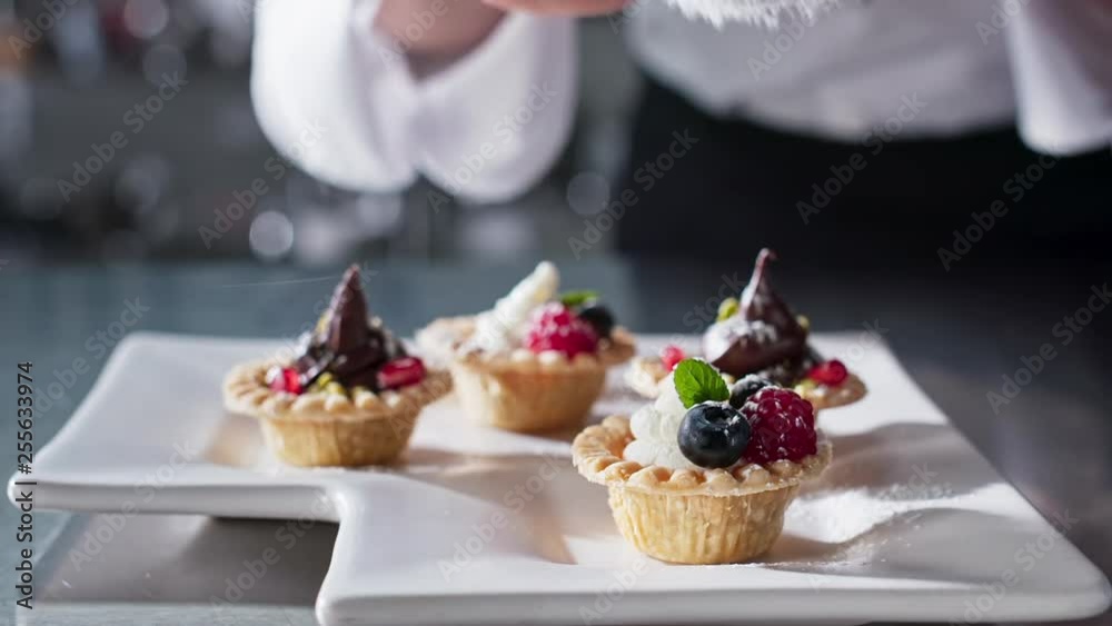 Chef sifts powdered sugar over small tarts Chef sifts powdered sugar over small tarts