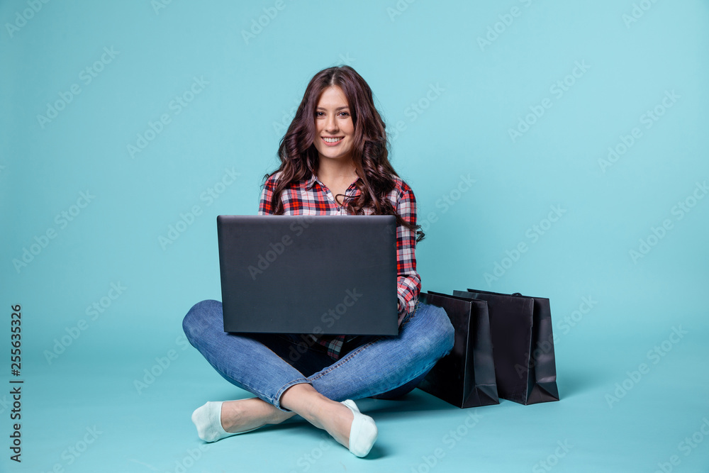 Naklejka premium Smiling brunette woman sitting on the flour with laptop and credit card to make online shopping