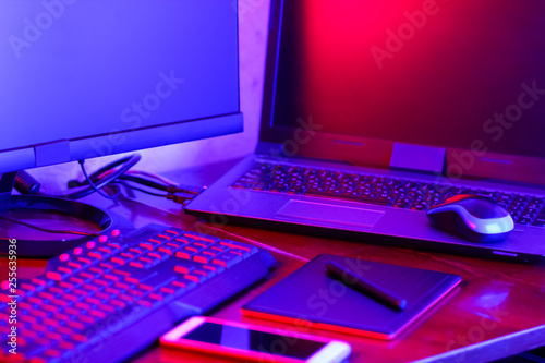 Workplace digital designer. Freelancer workplace in neon light. Computer, graphics tablet and smartphone on the table. Place for creativity in blue pink light