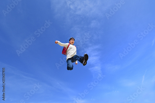 青空でジャンプする小学生の女の子（ランドセル）