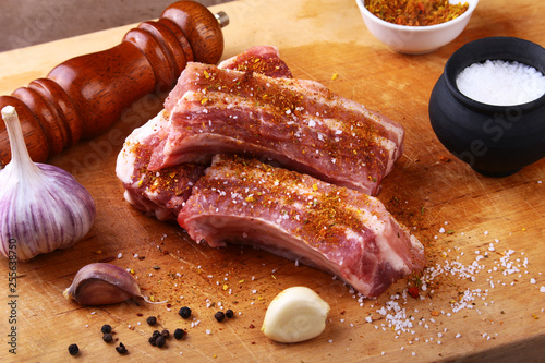 Raw ribs with a garlic, spices, ginger, salt and grinder on cutting board.