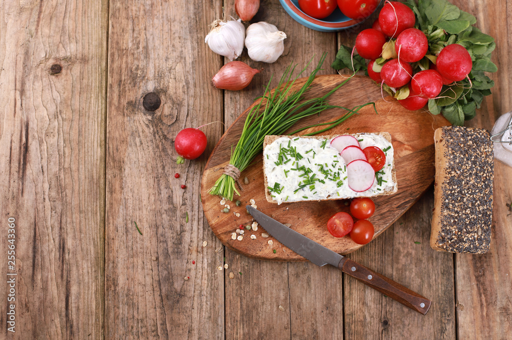 healthy breakfast -  wholemeal roll with quark and fresh chives, radishes and tomato on a rustic wooden table - healthy breakfast - top view