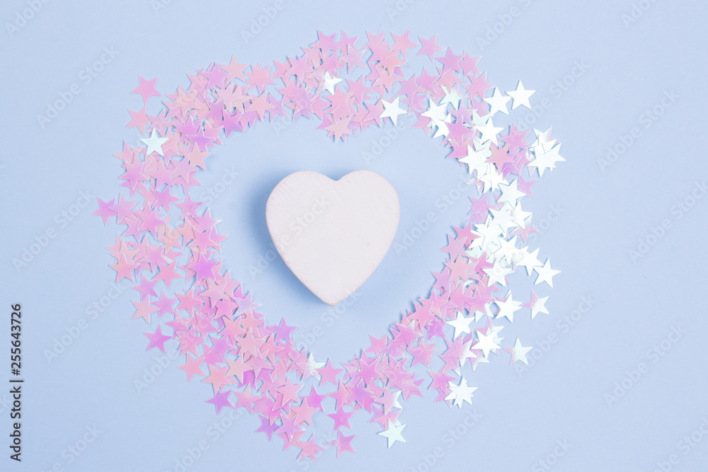 Decorative wooden heart with pink glitters on a pastel blue background.