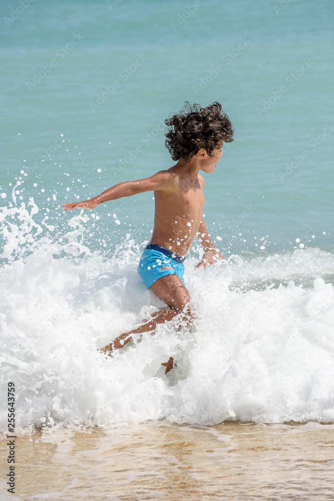 Happy kid playing on the beach in rough waters during a summer vacation Happy kid playing on the beach in rough waters during a summer vacation