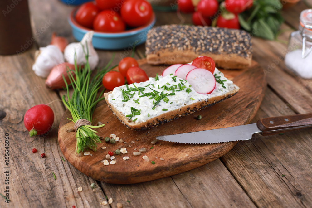 healthy breakfast -  wholemeal roll with quark and fresh chives, radishes and tomato on a rustic wooden table - healthy breakfast