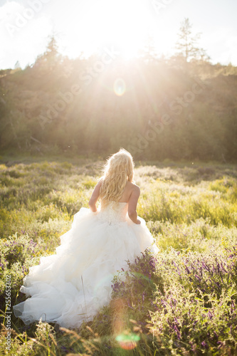 young bride holding up wedding dress and walking in field