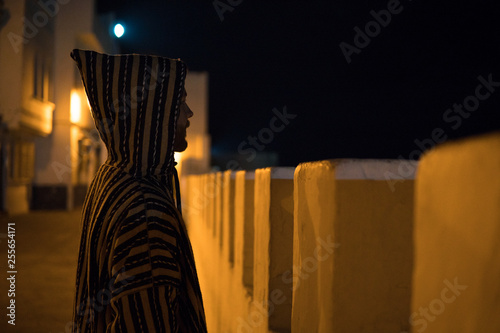 Man in Traditional moroccan djellaba on the Night street of Asilah Medina, on Atlantic Coast in Morocco photo