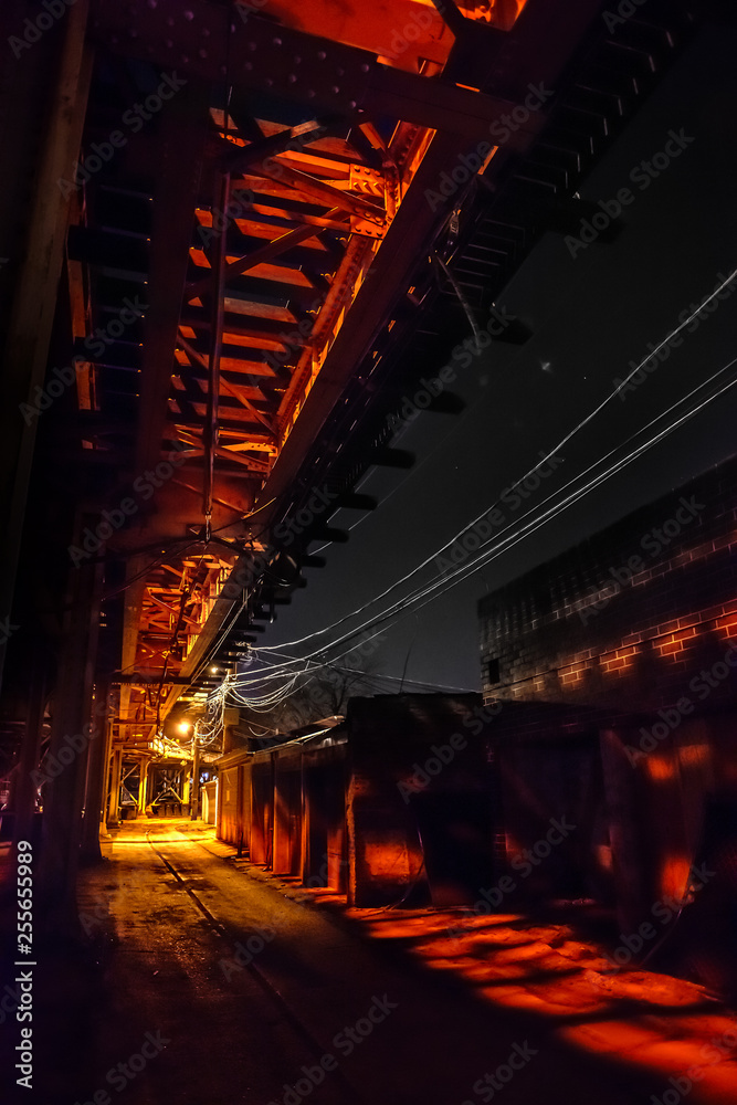 Fototapeta premium Scary urban city alley with elevated illuminated vintage railway tracks at night in Chicago