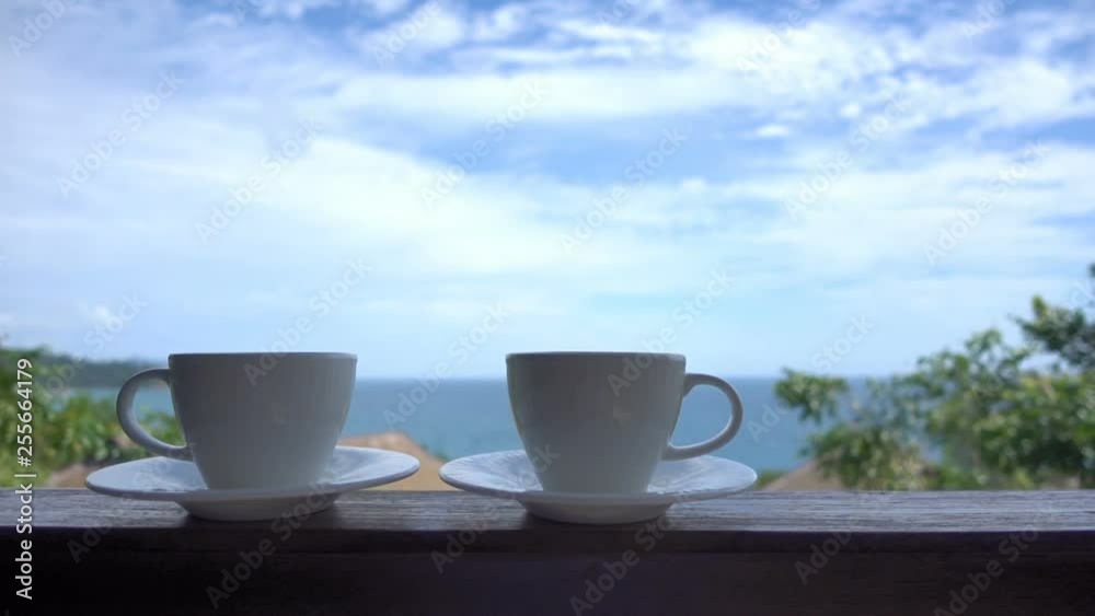 Two coffe cups on saucers sitting on a ledge in front of the ocean Two coffe cups on saucers sitting on a ledge in front of the ocean
