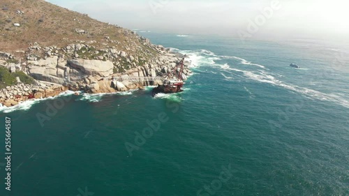 Beautiful shipwreck in Cape Town on the coast with ocean rocks and mountains, moving backwards and up, slowed down slightly. Medium to far distance away. photo