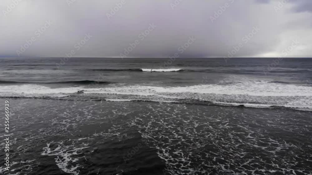 Drone flying out towards man catching a wave and surfing in. Surfing in the pacific northwest on a cloudy day Drone flying out towards man catching a wave and surfing in. Surfing in the pacific northwest on a cloudy day