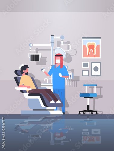 male arab dentist drilling teeth of man patient lying in dentistry chair professional dental office modern clinic interior arabic characters full length flat vertical