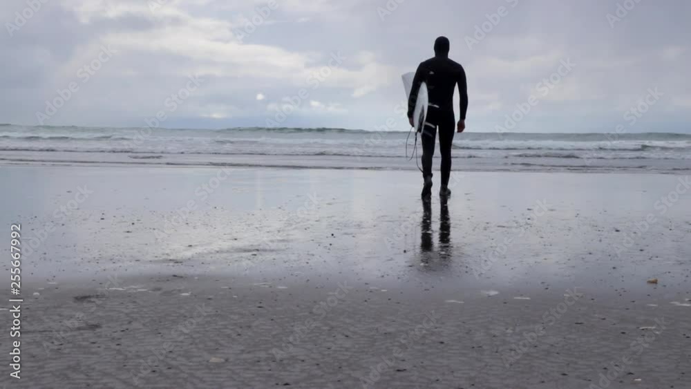 Man walking into the ocean with a surfboard and wetsuit on ready to surf. Slow motion walking on the beach. PNW Man walking into the ocean with a surfboard and wetsuit on ready to surf. Slow motion walking on the beach. PNW