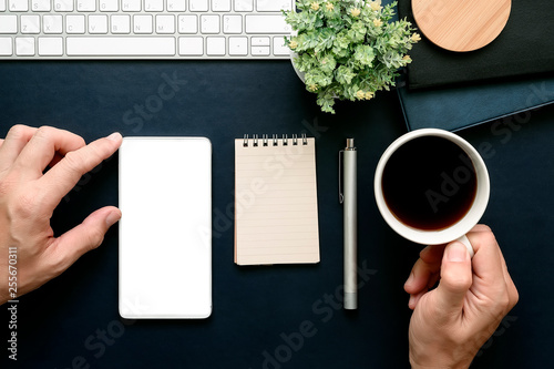 Shot of  man hand touching at screen of smartphone and holding cup of coffee while working at office.