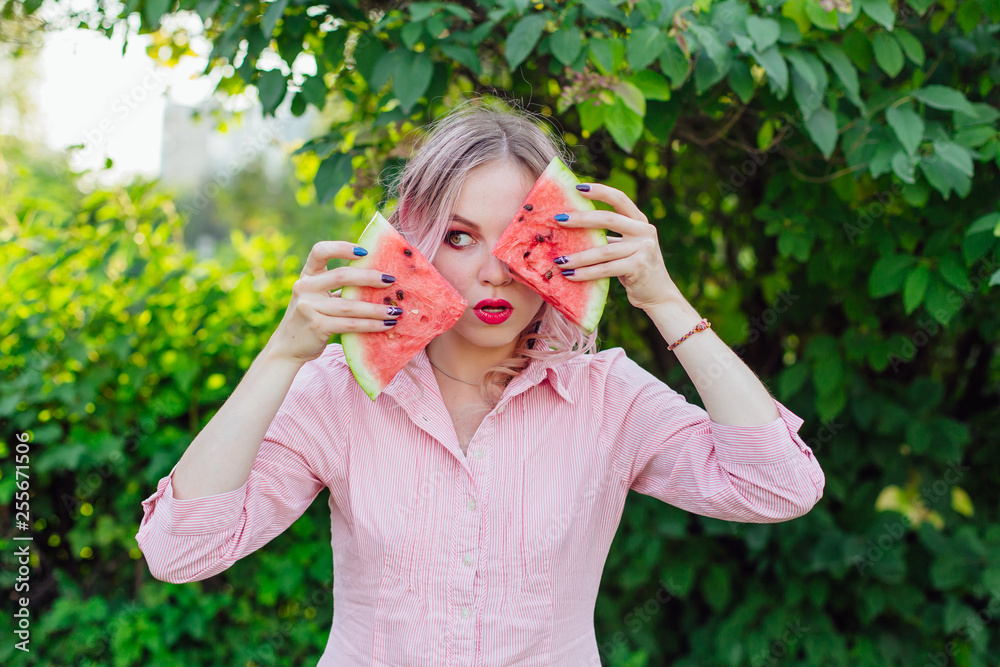 Beautiful young woman with pink hair holding two slices of watermelon in front of her face Beautiful young woman with pink hair holding two slices of watermelon in front of her face