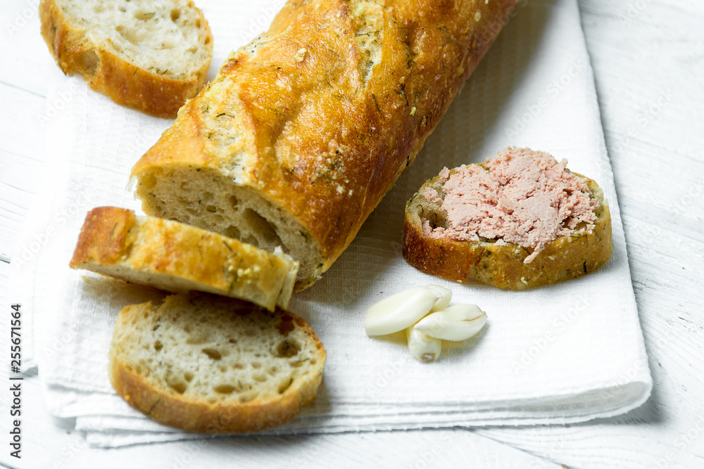 Obraz premium Garlic baguette with pate on white kitchen towel on wooden table.