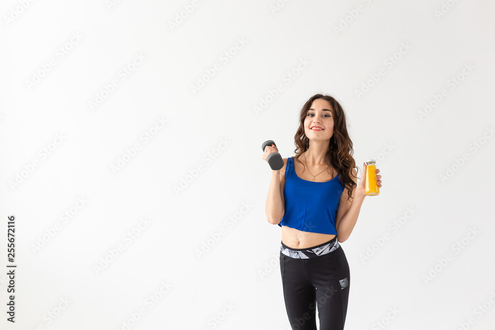 Sport, healthy lifestyle, people concept - young woman with a dumbbell in her hand and a bottle of juice in another hand on white background with copy space Sport, healthy lifestyle, people concept - young woman with a dumbbell in her hand and a bottle of juice in another hand on white background with copy space