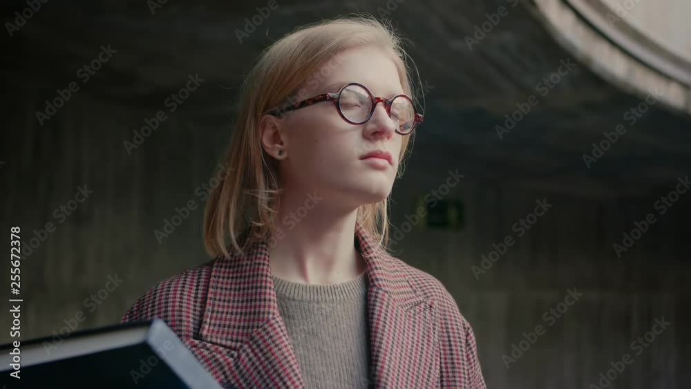 Close-up of young businesswoman, manager wearing glasses looking outside the camera successful motivated and professional female employer, adjusting her glasses, concrete background slow motion Close-up of young businesswoman, manager wearing glasses looking outside the camera successful motivated and professional female employer, adjusting her glasses, concrete background slow motion