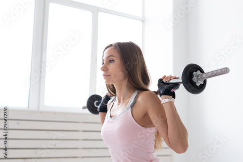 Fitness, sport, people concept - young woman in sport suit, gloves is squatting with bar