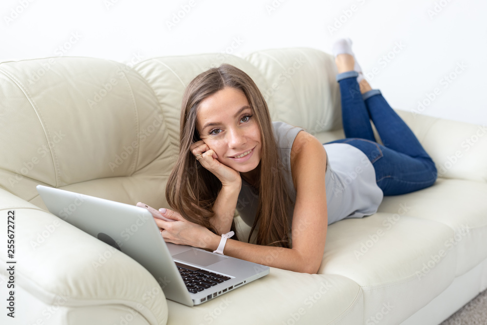 Technologies, freelance and people concept - pretty young woman lying on sofa with laptop and looking to the camera Technologies, freelance and people concept - pretty young woman lying on sofa with laptop and looking to the camera