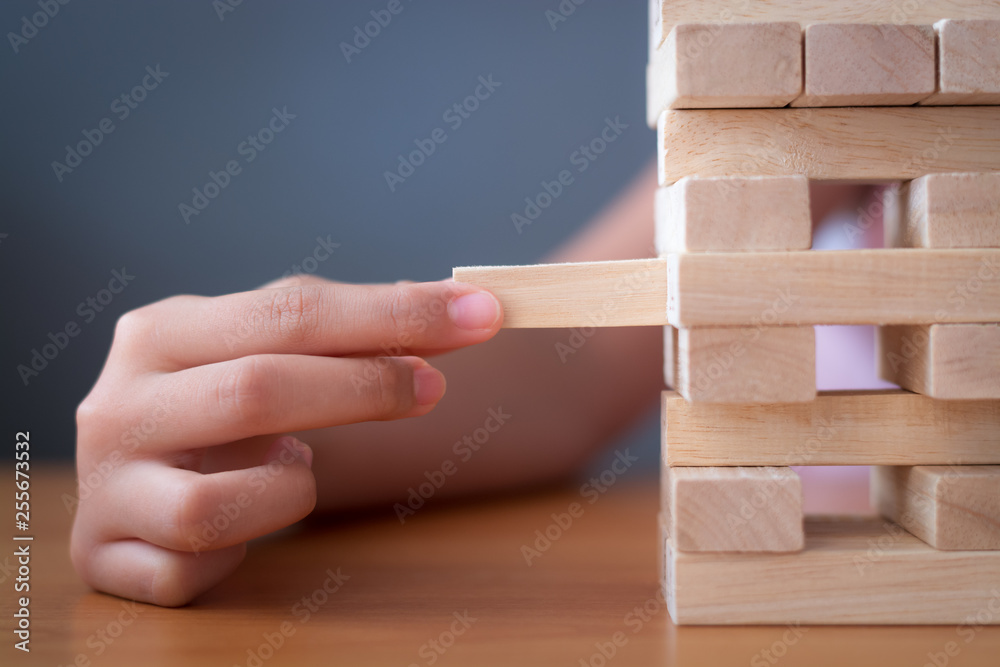 Hand of a girl placing and pulling wooden block on the tower.