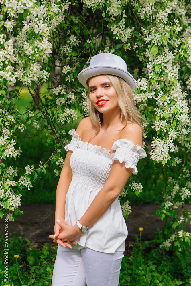 Fototapeta premium Sexy modern bride in white cylinder hat enjoing bloomin apple tree flowers.