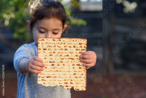 Portrait of the cute little girl holding matzah. Jewish child eating matzo (unleavened bread) in Jewish holidays Passover.